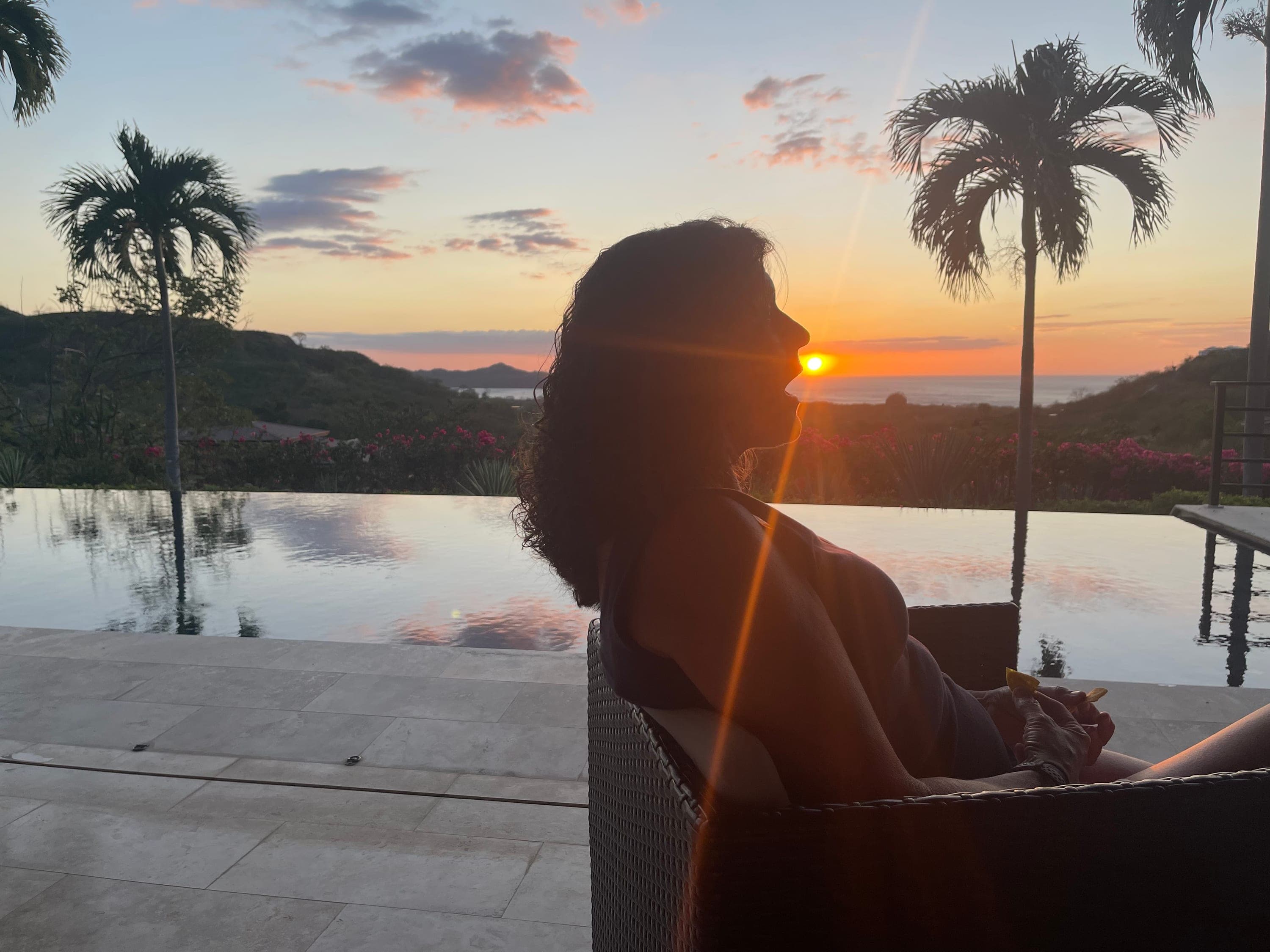 Silhouette by an infinity pool at sunset, palms framing the ocean horizon.