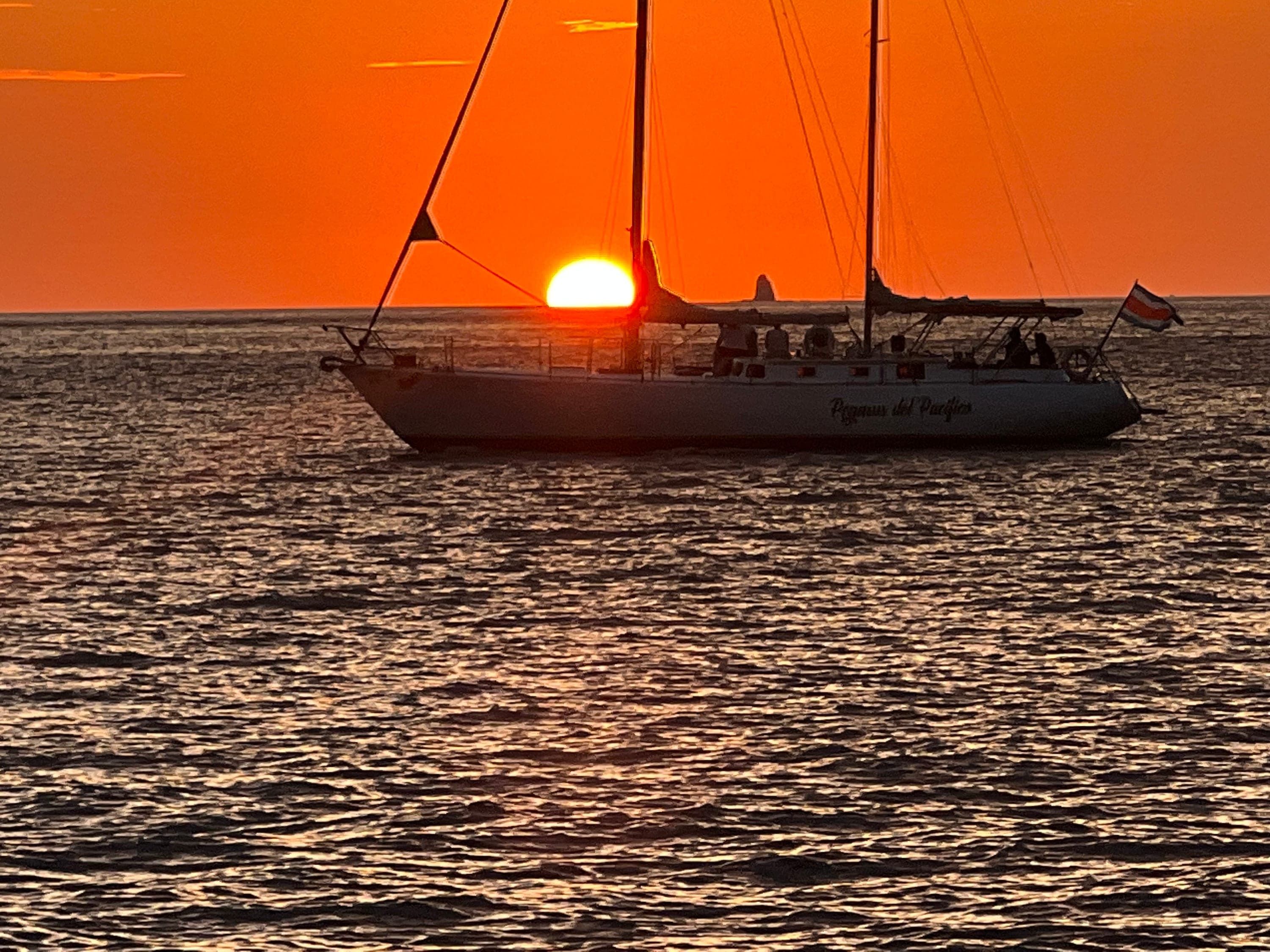 Sailboat silhouetted against an orange Pacific sunset.